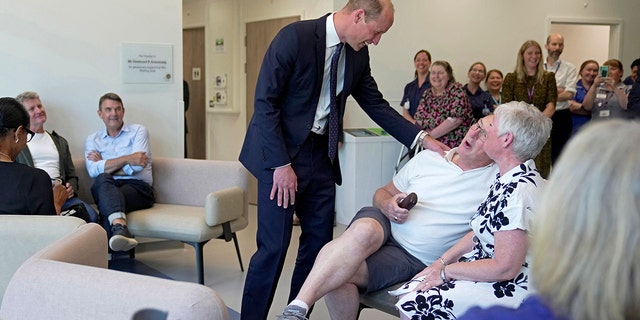 Prince William in a blue suit laughing with a man wearing a white shirt and shorts at a cancer centre