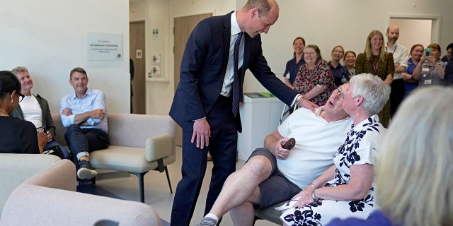 Prince William in a blue suit laughing with a man wearing a white shirt and shorts at a cancer centre