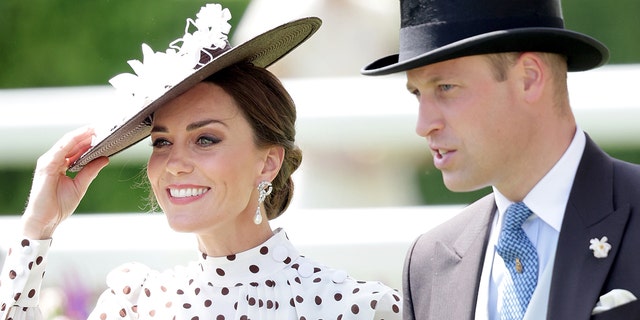Kate Middleton wearing a polka dot dress and a matching hat smiling next to Prince William in a grey suit and top hat