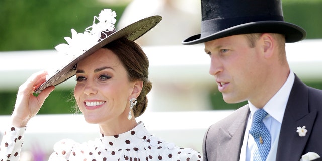 Kate Middleton wearing a polka dot dress and a matching hat smiling next to Prince William in a grey suit and top hat