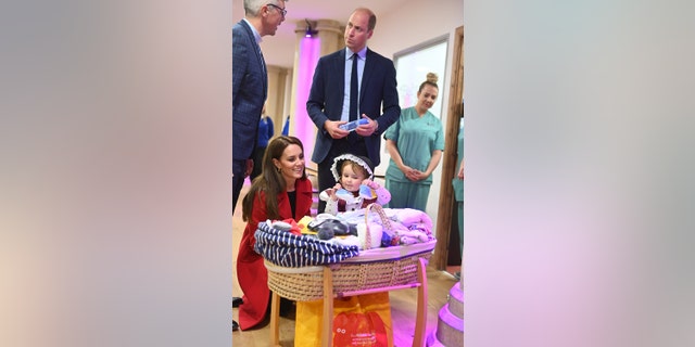 Kate Middleton wearing a red coat kneeling down next to a child