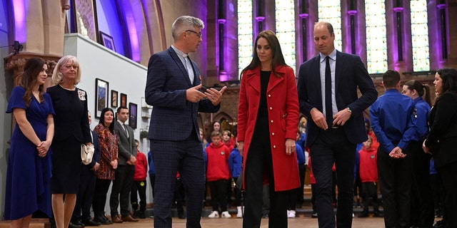 Prince William wearing a blue suit and Kate Middleton wearing a red coat inside St. Thomas Church