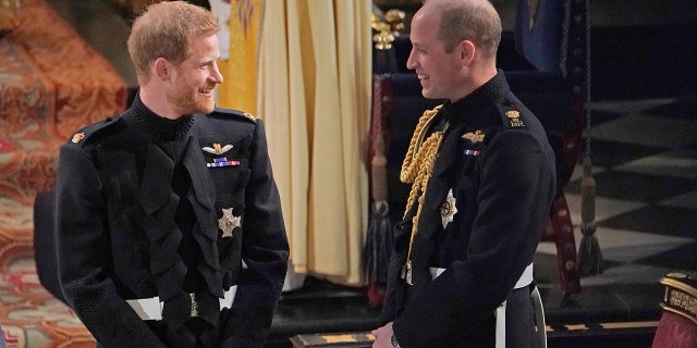 Prince William and Prince Harry smiling at each other wearing suits with medals