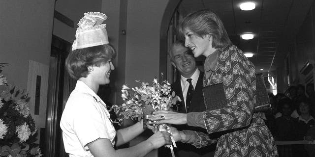 A black and white photo of Princess Diana receiving a bouquet of flowers from a nurse