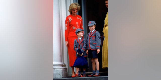 Princess Diana wearing red standing next to Prince William and Prince Harry in school uniforms