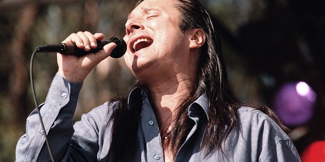 A close-up of Steve Perry singing wearing a blue shirt