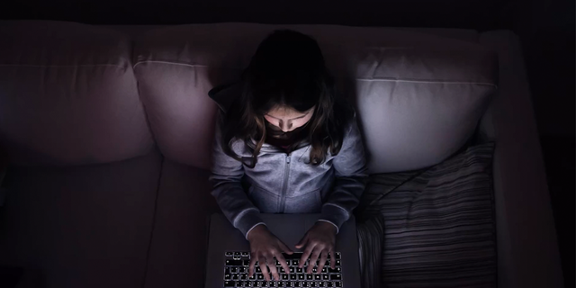 Little girl, sitting in a dark, playing with laptop .