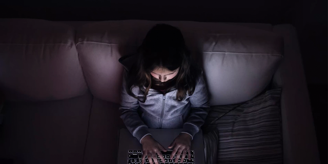 Little girl, sitting in a dark, playing with laptop .