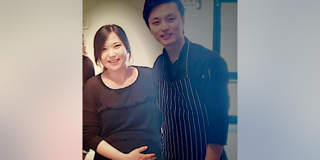 Eina Kwon holds her belly as she stands smiling next to her husbandd