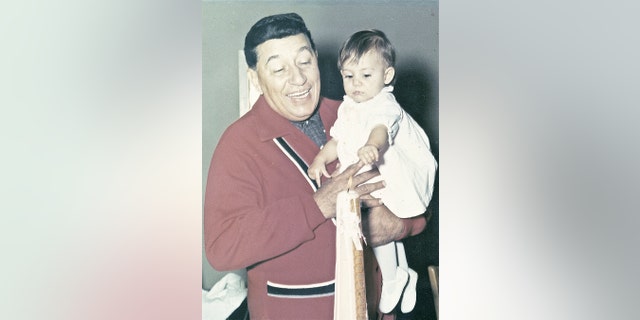 Louis Prima wearing a red sweater holding his daughter Lena
