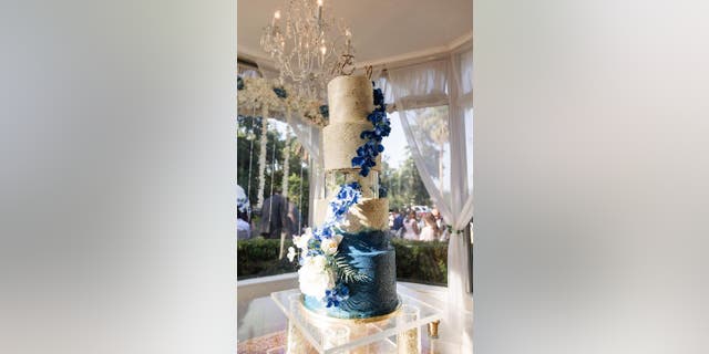 A blue and white wedding cake made by Lilly Mendoza sits on a cake table at a Florida hotel.