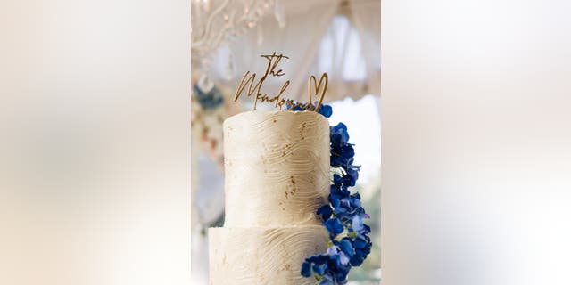 Top tier of a white wedding cake with a gold cake topper that says, 'The Mendozas.'