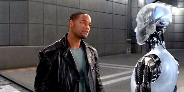 Will Smith in a black leather jacket as Del Spooner in "I, Robot" looking at a robot