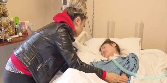 Lynn Fam stands over her daughter, who is in a hospital bed.