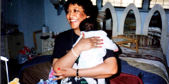 Minnie Smith smiling wearing a black shirt and holding an infant