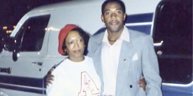 Minnie Smith wearing a white shirt and a red cap being held by her son