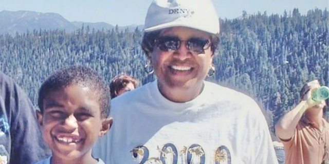 Minnie Smith wearing a white sweater and a white cap next to her grandson