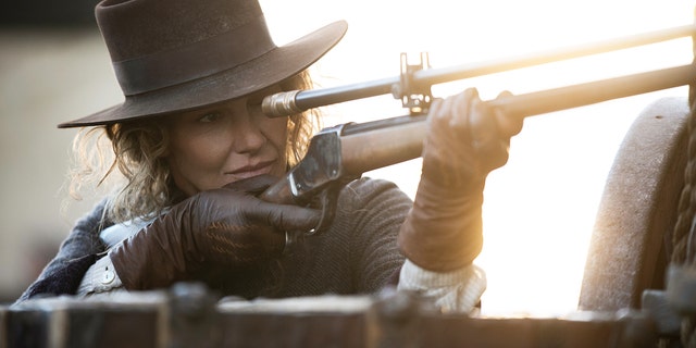 Faith Hill shooting a gun while wearing a cowboy hat.
