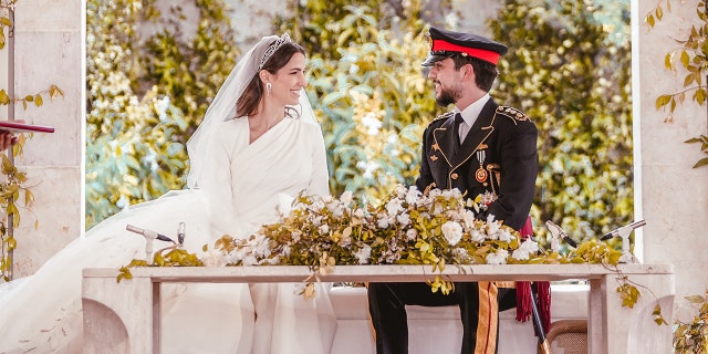 The royal bride and groom sitting together in front of a table with flowers