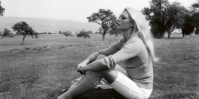 Brigitte Bardot wearing a sweater and white pants while sitting on the floor
