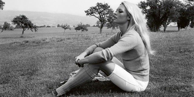 Brigitte Bardot wearing a sweater and white pants while sitting on the floor