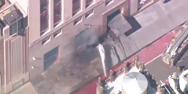 Firefighters shooting water toward smoke.
