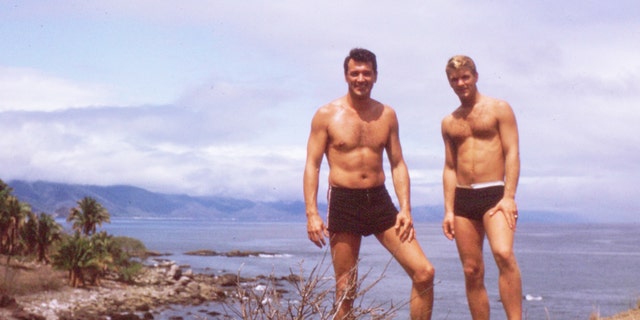 Rock Hudson on the beach with a male friend as they are both shirtless