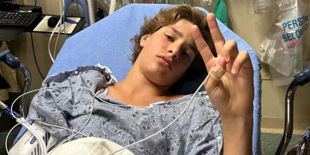 Gabriel Klimis flashing the peace sign from his hospital bed