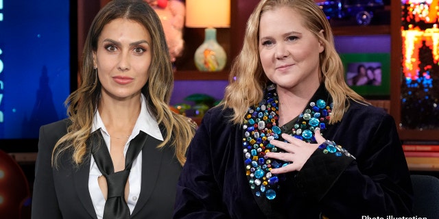 Amy Schumer holds her hand to her heart next to Hilaria Baldwin who wears a black suit