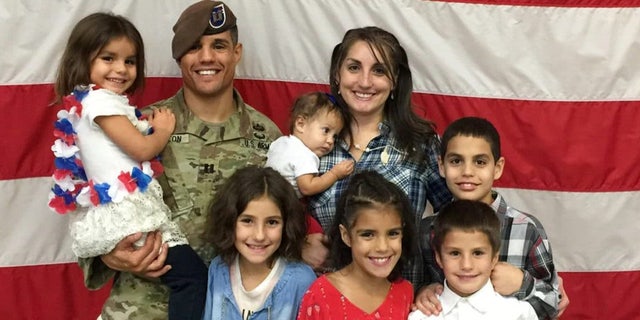 Army Capt. Gilberto De Leon stands in front of an American flag with his wife and children