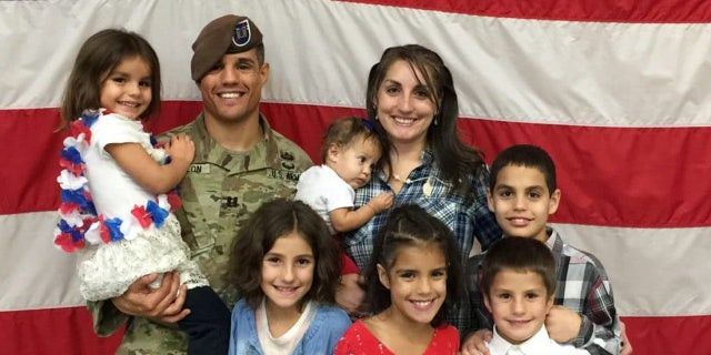 Army Capt. Gilberto De Leon stands in front of an American flag with his wife and children