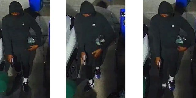 A man in a black hoodie and sweatpants holds a gun.