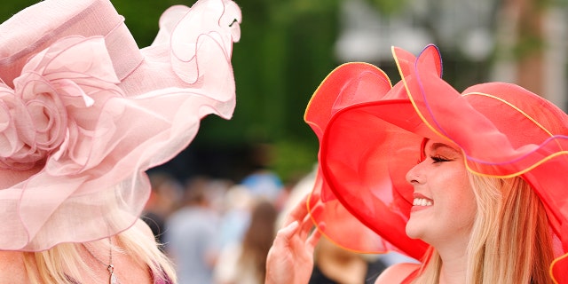 Two spectators wearing fancy, colorful hats for the Belmont Stakes