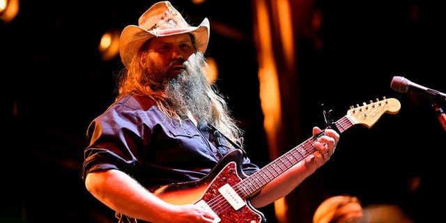 Chris Stapleton strums a guitar while on stage performing