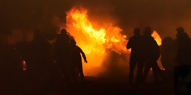 French rioters and police are hidden in shadow as a fire burns in the background during riots in Nanterre