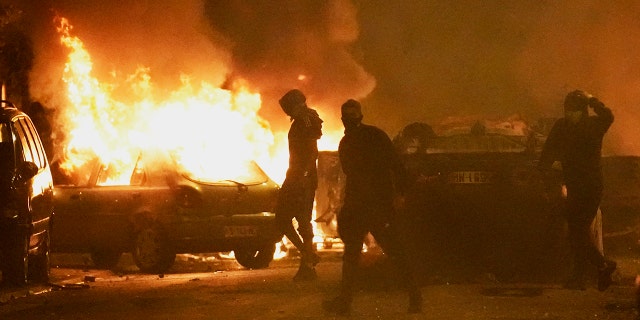 Rioters stand in front of burning vehicles during anti-police protests in France