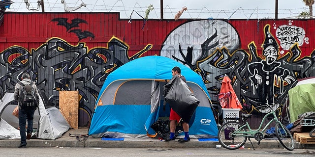 In the spring of 2023, two people walk in front of tents along a street in San Diego
