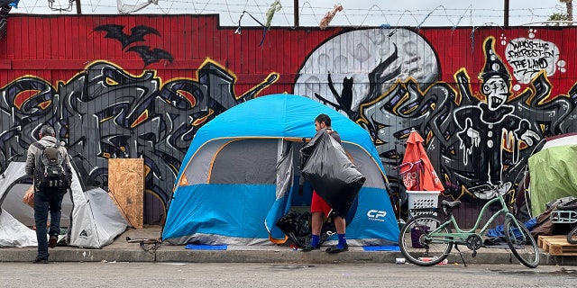 In the spring of 2023, two people walk in front of tents along a street in San Diego