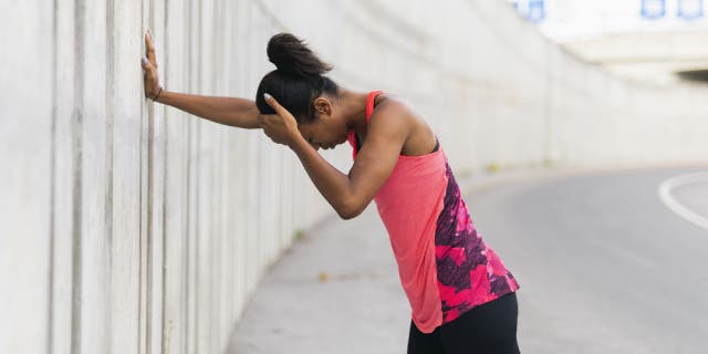 Woman holds onto concrete wall and appears to be dizzy.