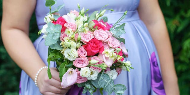 Pregnant bridesmaid wears periwinkle floral dress while holding a bouquet.
