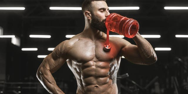 Male bodybuilder drinks from large water bottle.