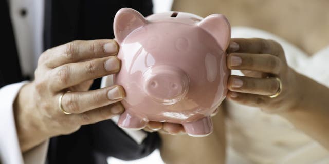 Bride and groom hold pink piggybank.