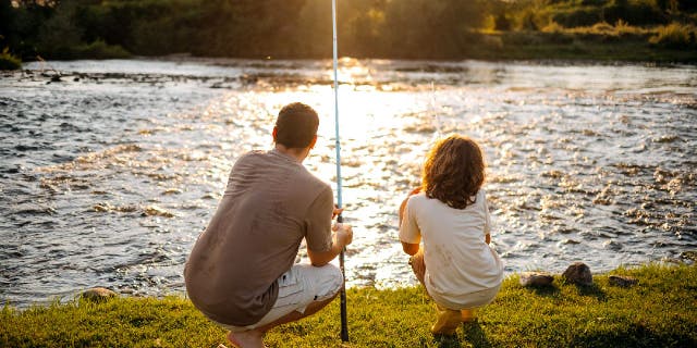 Father and child go fishing by shoreline.