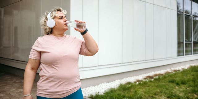 Woman in sportswear drinking water after outdoor workout.