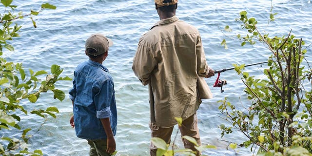 Father and son go fishing by shoreline.