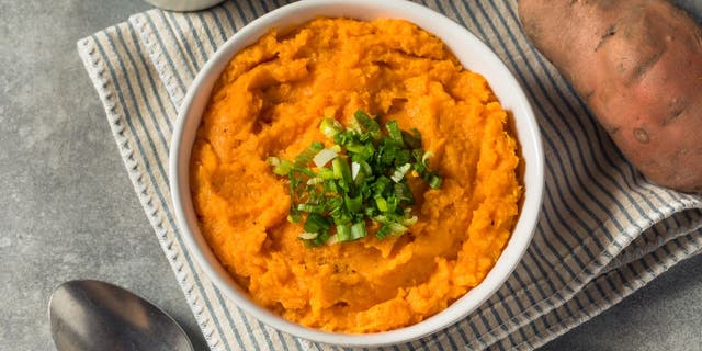 Mashed sweet potatoes served in a dish with green herbs.