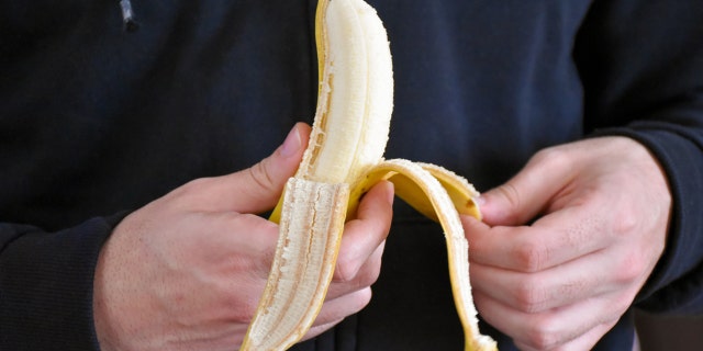 A closeup image of a man's hands peeling a banana.