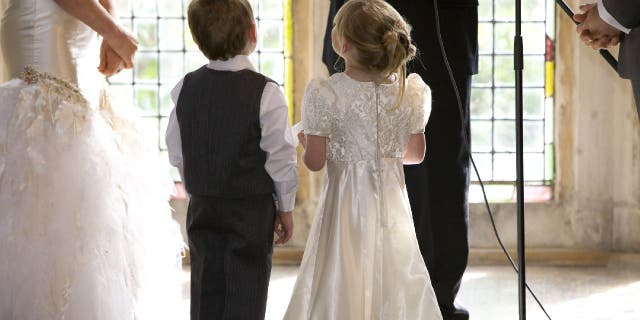 A ring bearer and flower girl stand at an altar with the bride and groom.