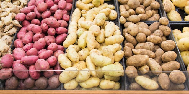 Grocery store displays different colors and varieties of potatoes for people to select.