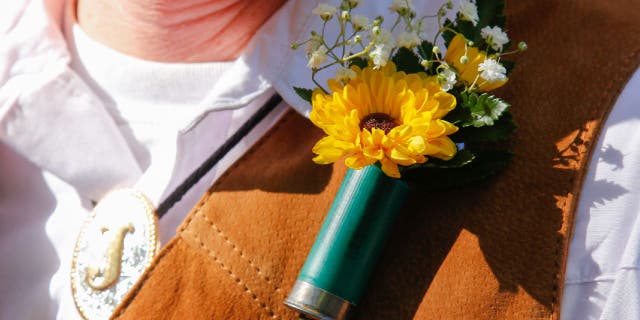 Man wears shotgun boutonniere in what appears to be a cowboy-themed wedding.